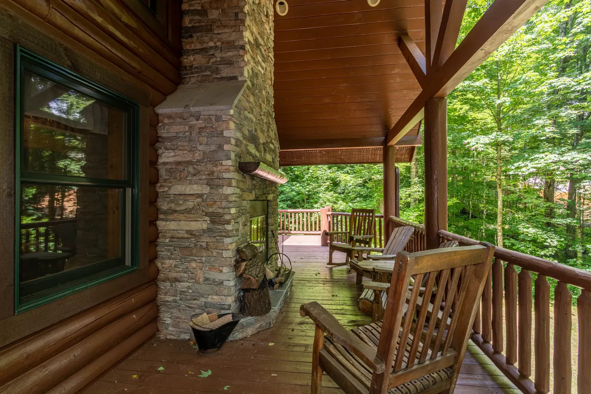 A rustic stone outdoor fireplace with wooden chairs set against a backdrop of abundant greenery. The natural surroundings evoke a sense of peace and privacy, ideal for relaxing or socializing outdoors.