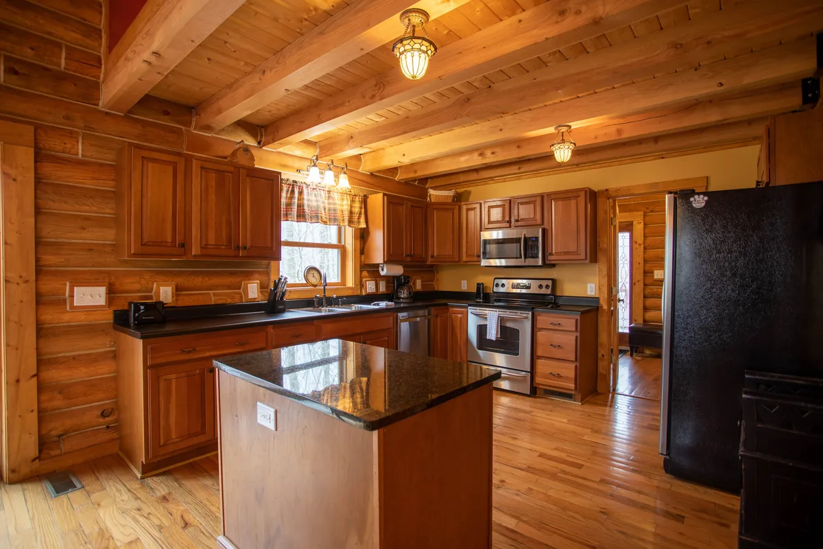 A warmly lit kitchen featuring a spacious island, stainless steel appliances, gleaming wooden cabinetry, and elegant lighting fixtures. The room feels inviting, emphasizing both the functionality and style perfect for preparing meals and entertaining guests.