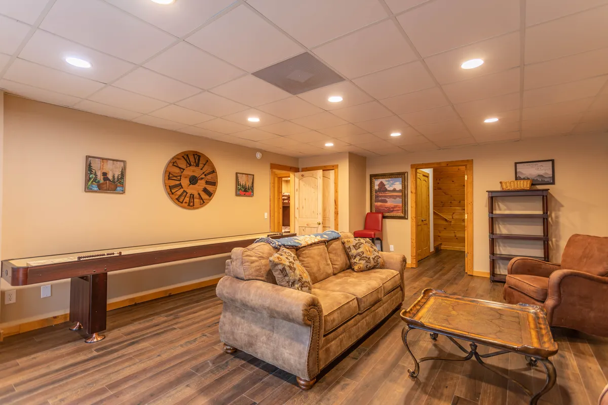 This image displays a cozy lounge featuring a sofa, a prominent shuffleboard table, wall clock, and artwork on the wall. The seating area is inviting, suggesting a perfect space for relaxing and engaging in friendly games.