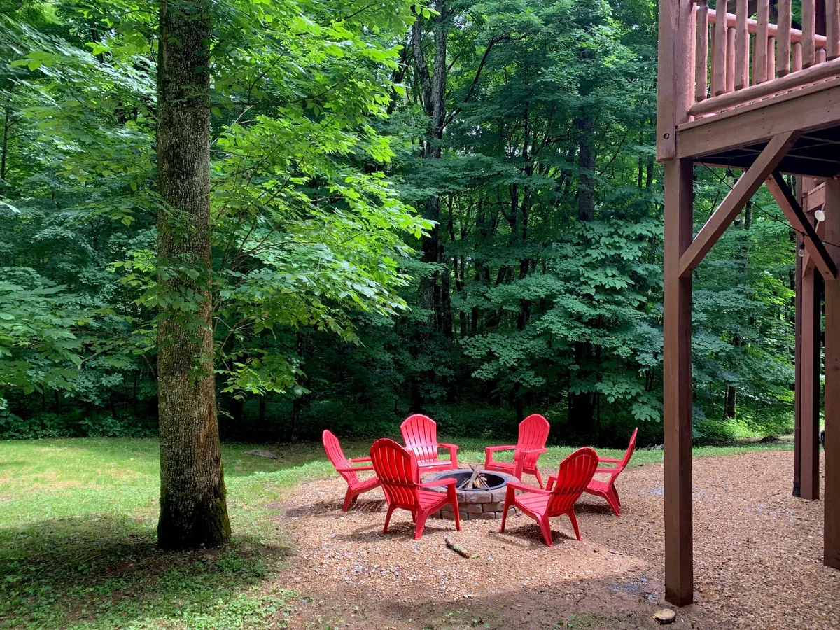 This image showcases an inviting outdoor fire pit, encircled by red Adirondack chairs and nestled amongst tall trees. The communal seating area sets the stage for storytelling, roasting s'mores, and sharing memorable moments under the stars.