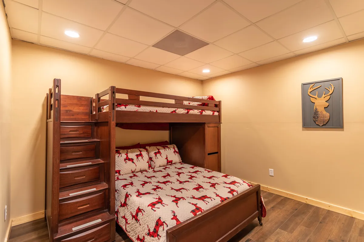 A playful, family-friendly bedroom with a sturdy wooden bunk bed adorned in red reindeer-patterned bedding, warm wooden furnishings, and whimsical deer wall art. The room is cozy, inviting, and well-suited for children or teens.