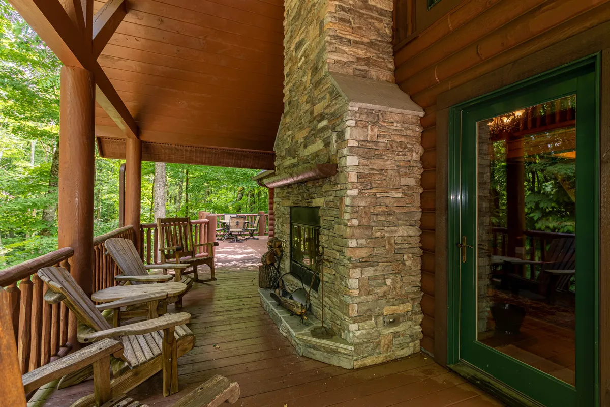 An inviting wooden deck outfitted with stone fireplace, classic rocking chairs, and lush greenery in the background. The scene exudes warmth and encourages group relaxation, with hints of conversation and shared quiet moments as the sun sets beyond the trees.