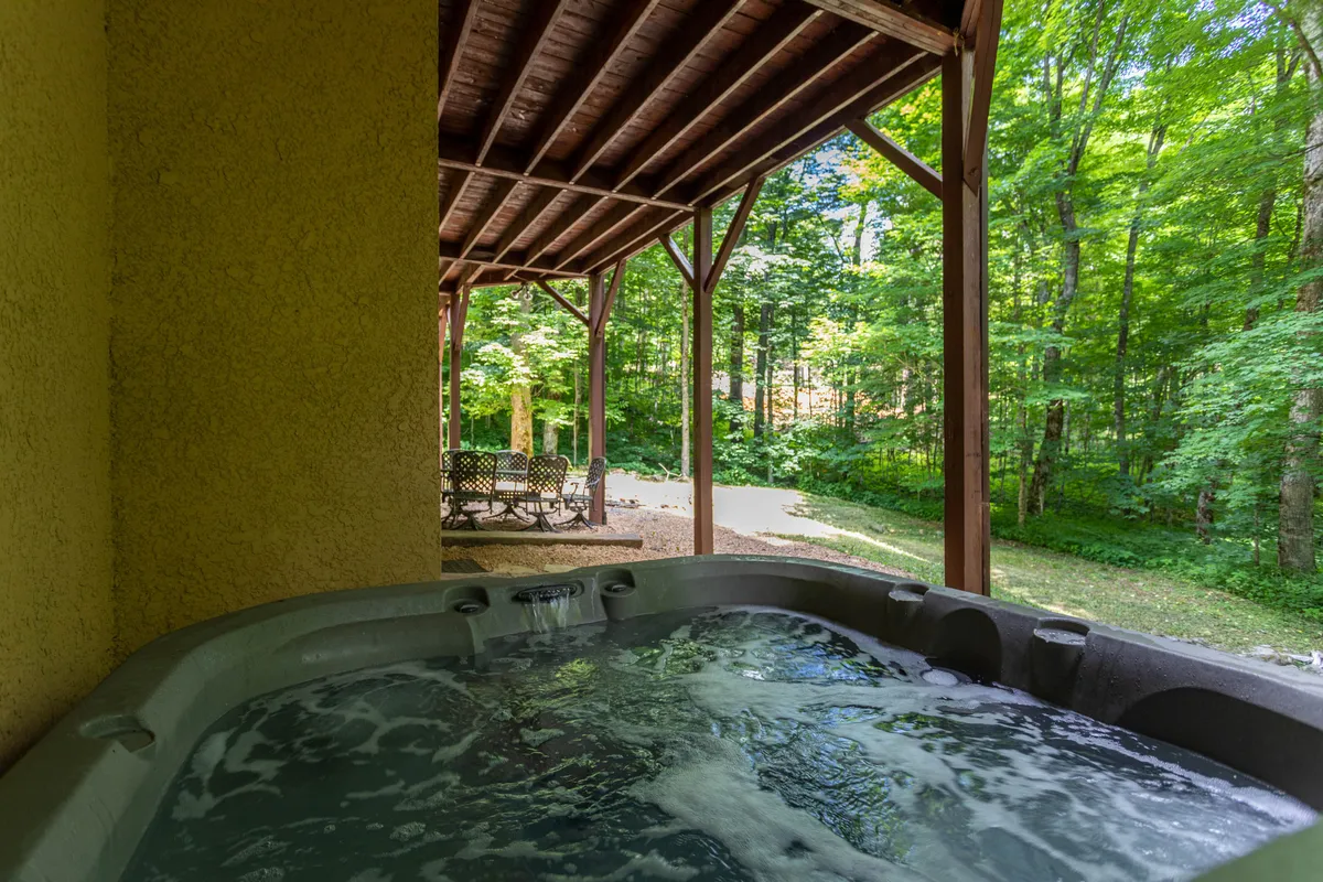 An exterior shot showing the brand new hot tub nestled among wooden beams and surrounded by trees. Patio furniture creates a comfortable spot for socializing and relaxing right outside the lounge area.