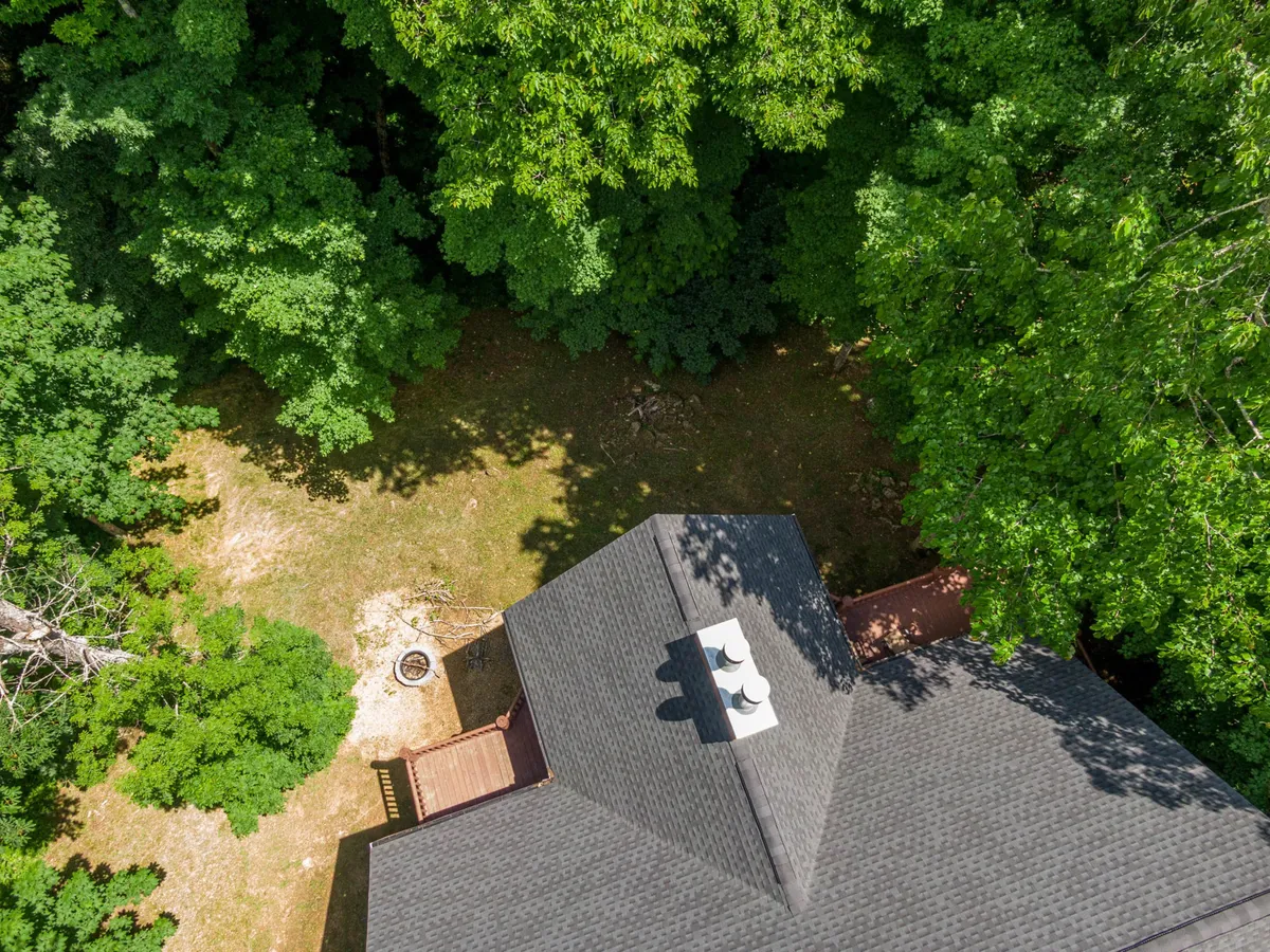 A wide exterior view of the house's roof, framed by towering trees and an inviting outdoor space, suggesting proximity to nature and privacy. The scene conveys the home’s harmonious integration into its scenic mountain surroundings.