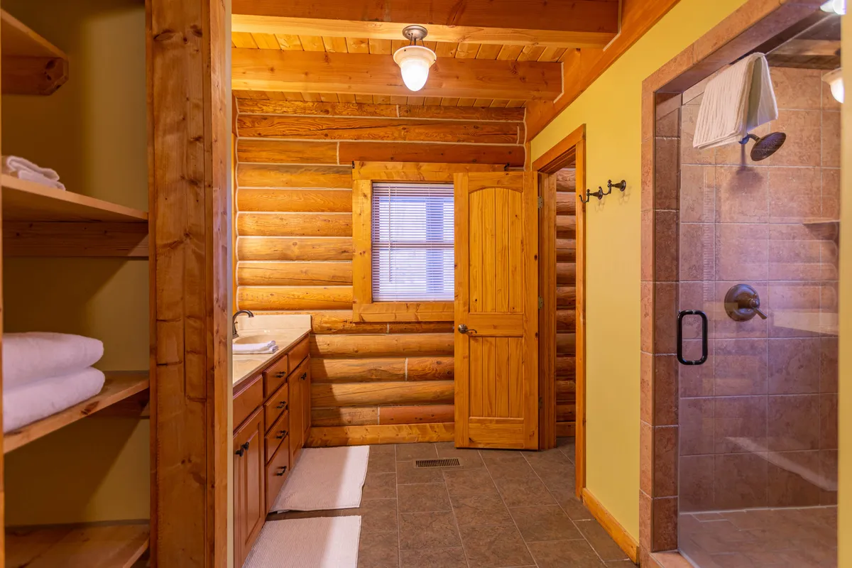 A tranquil bathroom with wooden walls, a vanity with a sink, a spacious shower area, and a window that brings in natural light. The mood is peaceful and spa-like.