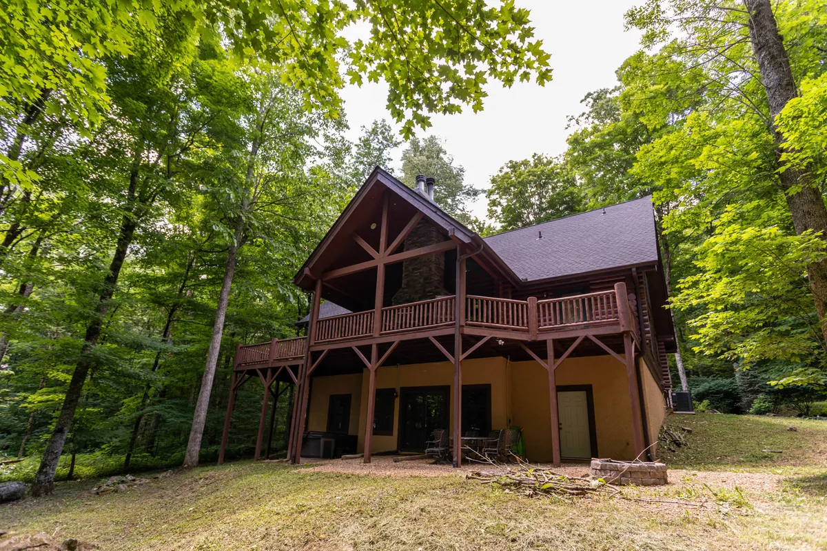 A serene view of the wooden balcony and stone chimney, surrounded by tall trees and nature. The balcony offers a peaceful place to relax after outdoor activities, with the home’s large windows connecting the indoors to the scenic environment.
